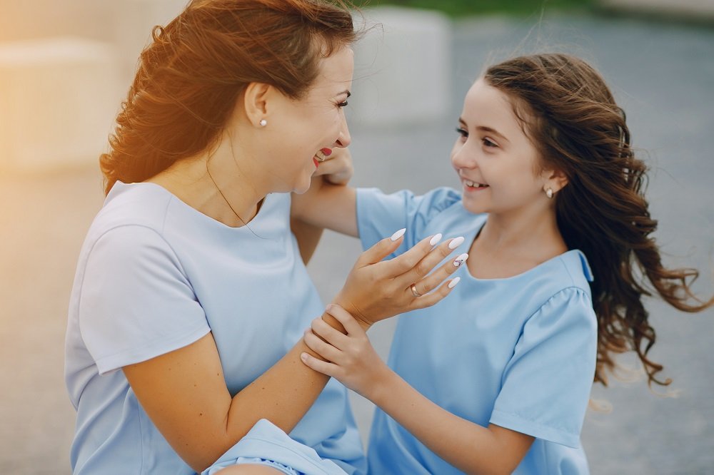 A mother and daughter joyfully playing together outdoors, both wearing matching blue dresses.